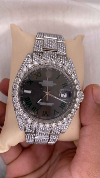 Side view of luxury iced out moissanite watch with full diamond bezel and band, black dial, and green Roman numerals.