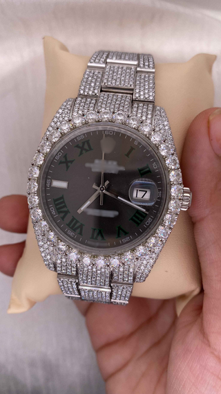 Side view of luxury iced out moissanite watch with full diamond bezel and band, black dial, and green Roman numerals.