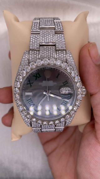 Side view of luxury iced out moissanite watch with full diamond bezel and band, black dial, and green Roman numerals.