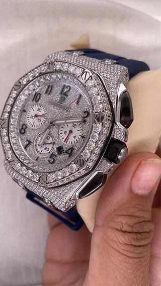 Side view of a men’s moissanite watch with a diamond-studded bezel, silver case, and blue strap, shown on display.