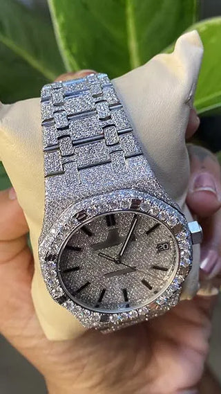 Angled view of a men’s VVS moissanite watch, fully iced out with sparkling stones, held in hand with green leaves behind.