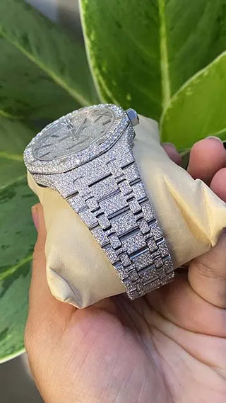 Side view of a men’s VVS moissanite watch, fully iced out with shimmering stones, held in hand against green leaves.