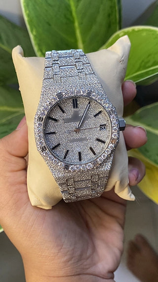 Men’s VVS moissanite watch fully iced out with shining stones, shown in hand with green leaves in the background.