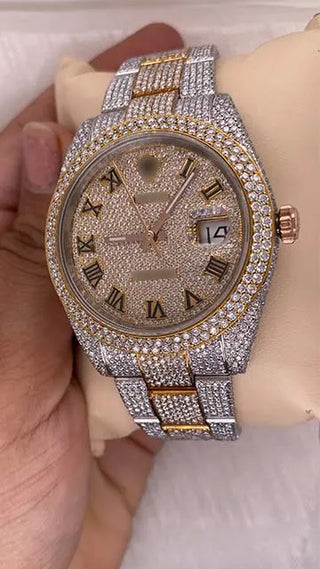 Angled view of a moissanite watch with a gold-tone Roman numeral dial, date window, and fully studded bezel and strap.