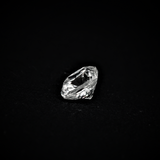 Side view of a cushion-cut moissanite placed on a black textured surface, revealing its depth, pavilion, and faceted brilliance.