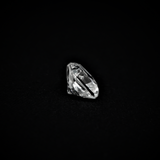 Side view of a cushion-cut moissanite placed on a black textured surface, revealing its depth, pavilion, and faceted brilliance.