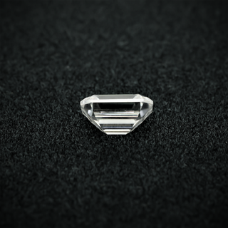 Back view of an emerald cut moissanite resting on a black textured surface, showcasing the culet and step-cut pavilion facets with sharp clarity.
