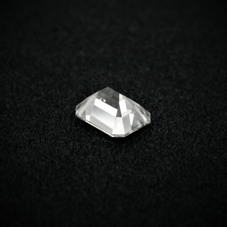 Back view of an emerald cut moissanite resting on a black textured surface, showcasing the culet and step-cut pavilion facets with sharp clarity.