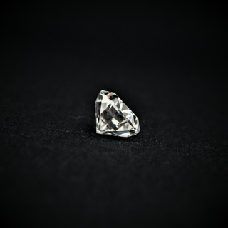 Side angled view of a loose round brilliant-cut moissanite resting on a black surface, highlighting its faceted profile.