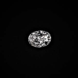 Front view of oval cut moissanite held in tweezers, reflecting sharp brilliance and flawless symmetry on black backdrop.