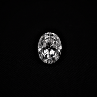 Front view of oval cut moissanite held in tweezers, reflecting sharp brilliance and flawless symmetry on black backdrop.